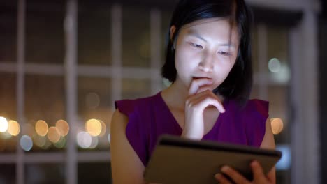 Thoughtful-asian-businesswoman-using-tablet-by-office-window-at-night,-slow-motion