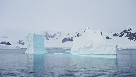 Big-Iceberg-Ice-Formations-Aerial-drone-shot-Floating-on-the-Ocean-Sea-Water-in-Antarctica-Scenery,-Antarctic-Peninsula-Mountains-Landscape-Covered-in-Snow-and-Snowy-Winter-Weather,-Southern-Ocean