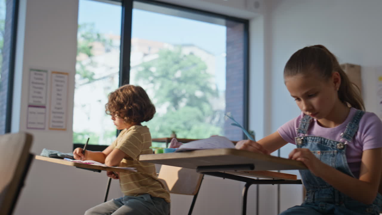 Elementary school pupils writing in copybooks sitting desks. Group classmates