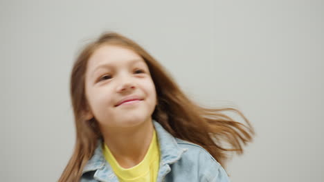 playful toddler under bright lights moves head sideways with cheerful expression while wearing denim jacket, showing innocence and happiness in candid moment during daily activity
