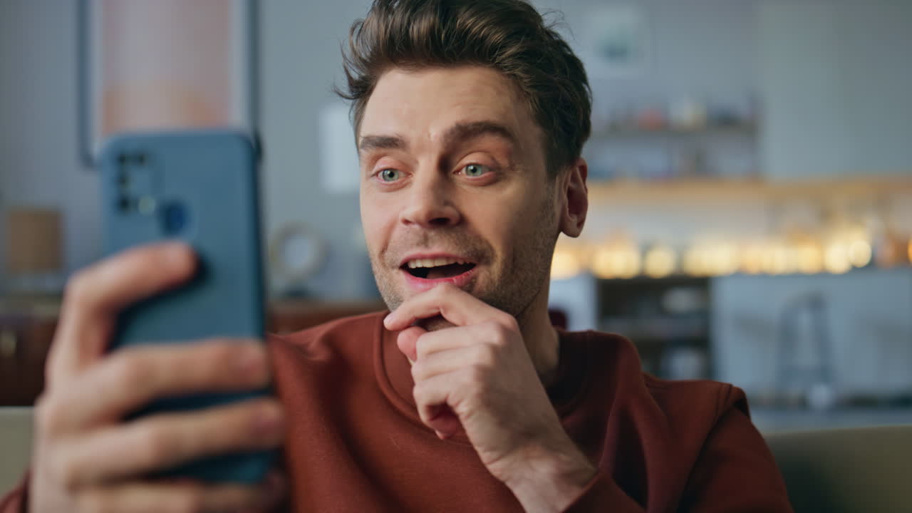 Laughing man enjoy videocall by cellphone sitting apartment couch alone close up