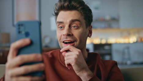 laughing man enjoy videocall by cellphone sitting apartment couch alone close up