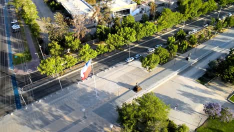 aerial orbit of the chilean flag waving in vitacura's bicentennial park with people walking on their walkways - drone shot