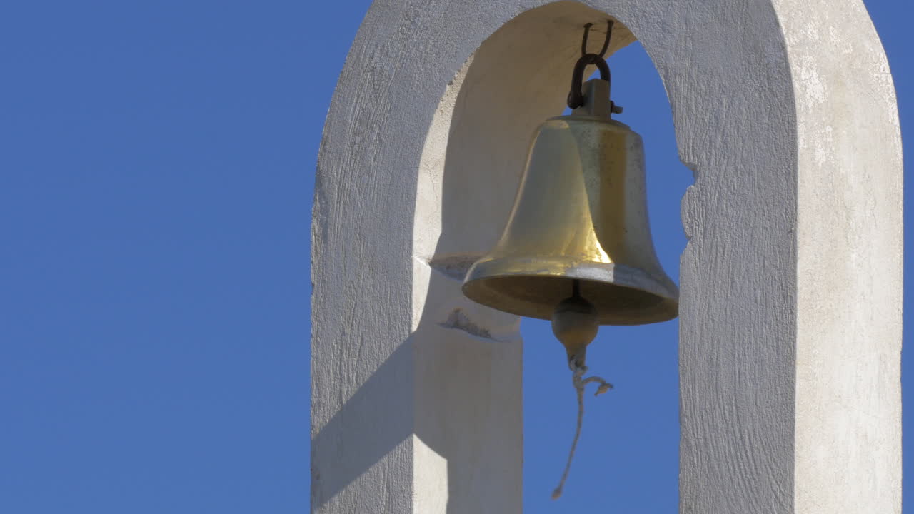 On a semicircular concrete arch hangs a bell and swinging in the wind