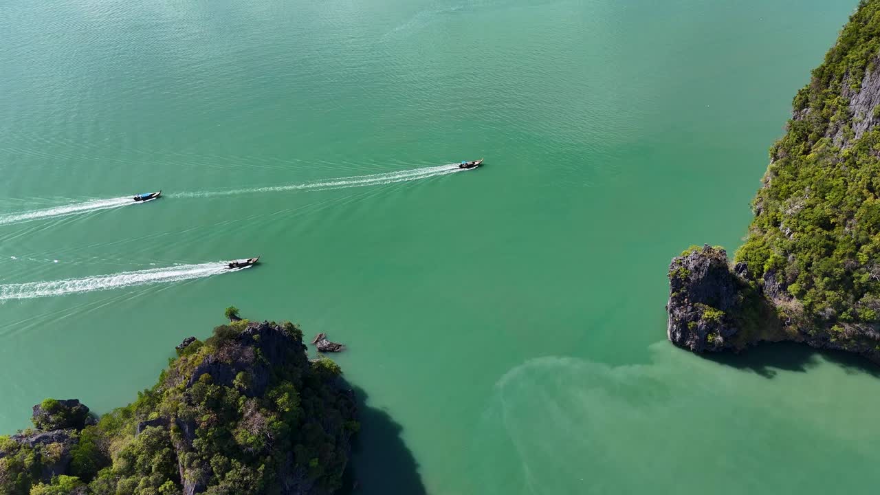 Drone footage captures boats navigating turquoise waters around lush islands in Phang Nga Bay, Thailand, under bright sunlight