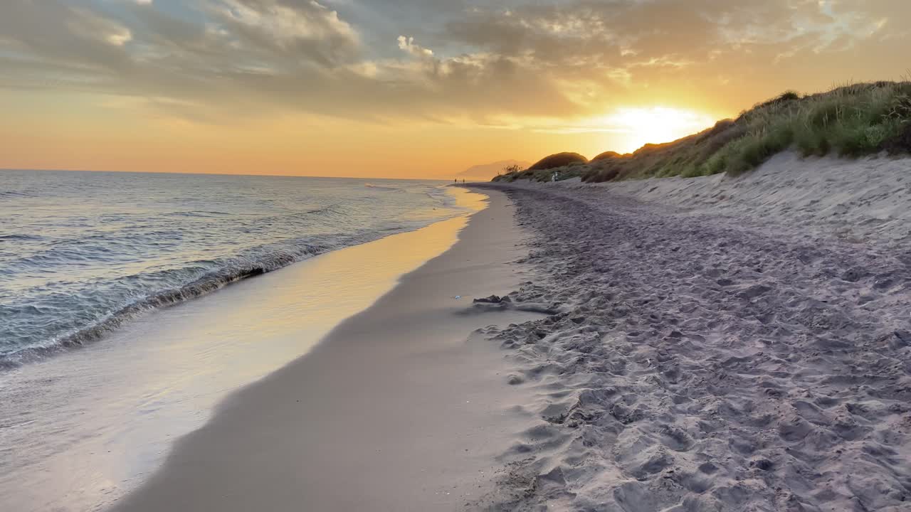 Walking along the shore of a beach under a warm and magical sunset in southern Spain.