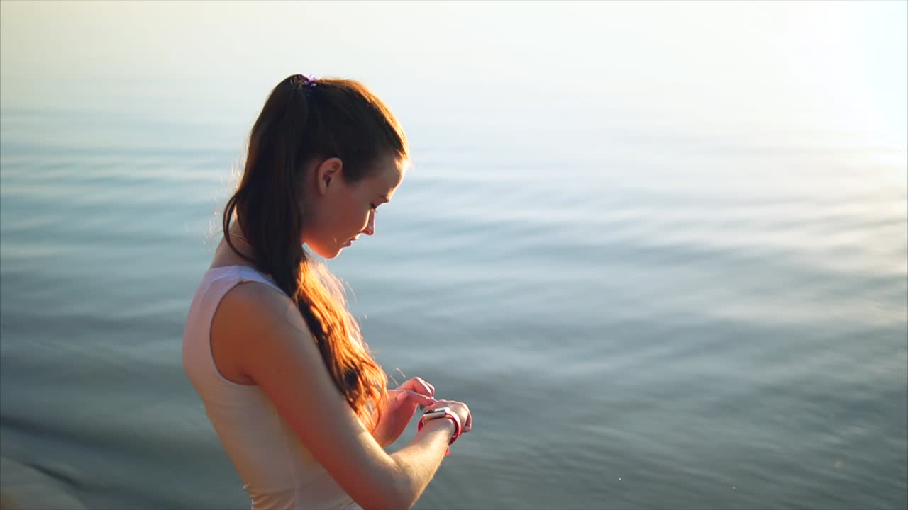 Woman checking smartwatch by the lake at sunrise