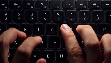 close up and top view footage of young businessman hands busy working, searching and studying by typing on glowing keyboard in the dark for send emails and surf on a web browser