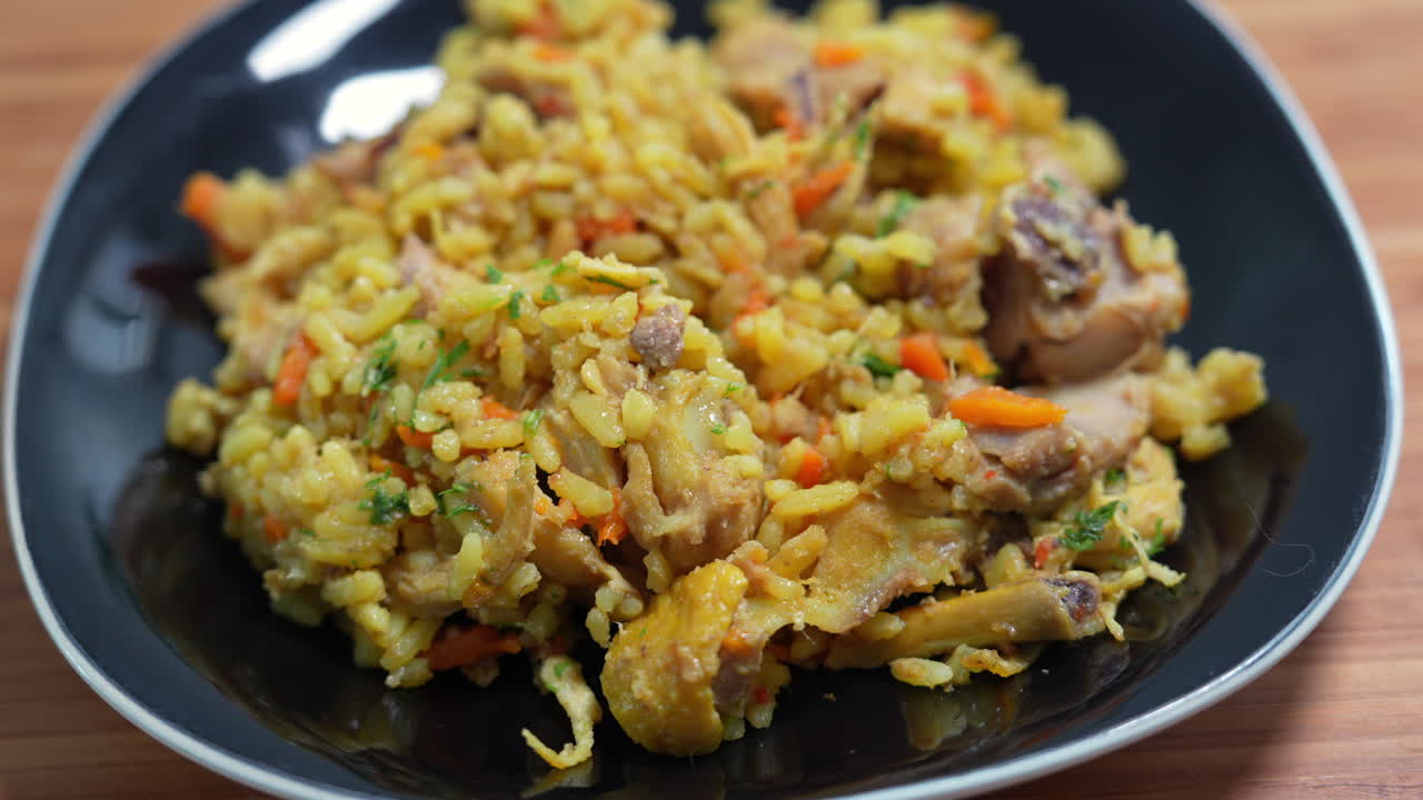 Deliciously seasoned Colombian rice with chicken, carrots, and herbs served on a sleek black plate. Vibrant colors and textured ingredients captured in a detailed, intimate view