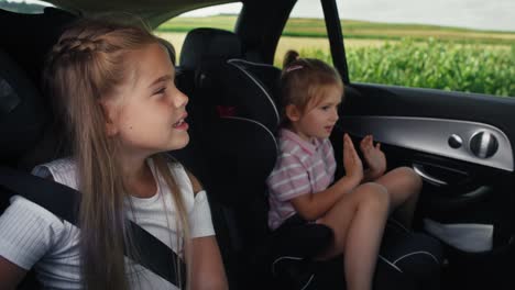 Two-caucasian-female-children-riding-in-the-car-in-the-back-seat-and-singing.