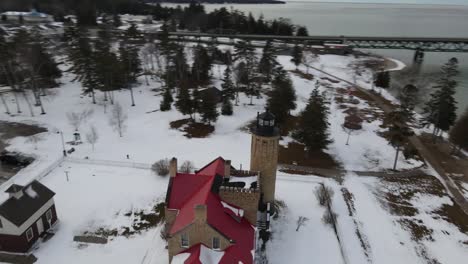 Tiro-De-Dron-Giratorio-Del-Antiguo-Faro-De-Mackinac-Point-Que-Gira-Para-Mostrar-El-Puente-Mackinac-En-La-Ciudad-De-Mackinaw,-Michigan-En-El-Invierno