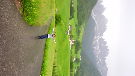 Man-wearing-a-hat-twirls-joyfully-amidst-the-lush-greenery-of-Val-di-Funes,-reveling-in-the-rain