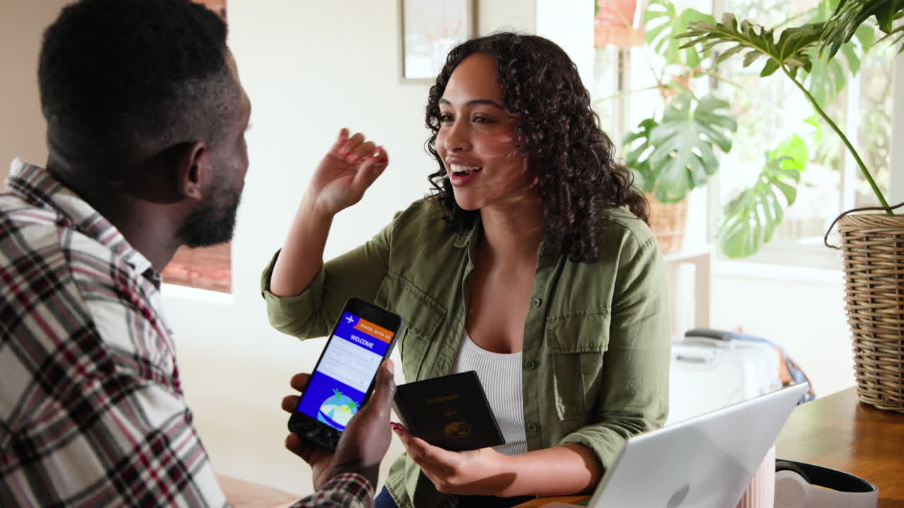 Multiracial couple planning travel with passport and laptop, smiling at home