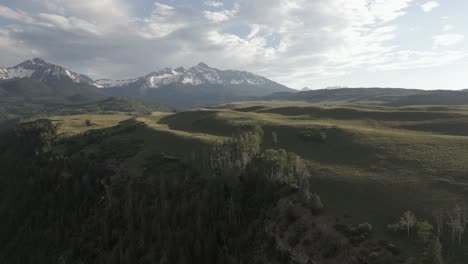 Aerial-ascends-low-rock-bluff-to-grassy-plateau-meadow-in-CO-mountains