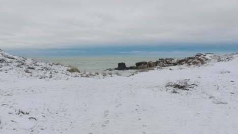 Aerial-establishing-view-of-abandoned-seaside-fortification-buildings-at-Karosta-Northern-Forts-on-the-beach-of-Baltic-sea-,-overcast-winter-day,-wide-drone-shot-moving-forward-low