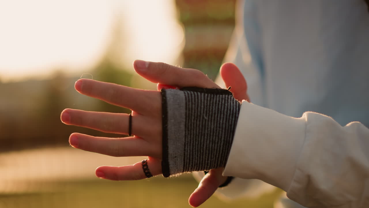 Nahaufnahme von Händen, die unter dem Gegenlicht des Sonnenuntergangs einen fingerlosen Handschuh anpassen, wobei Bewegung und Geschicklichkeit hervorgehoben werden, während sich die Finger dehnen und beugen. Intime Probenaufnahme, die Rhythmus, Präzision und künstlerisches Aufwärmen festhält