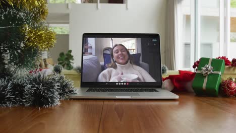 Smiling-caucasian-woman-drinking-coffee-on-christmas-video-call-on-laptop