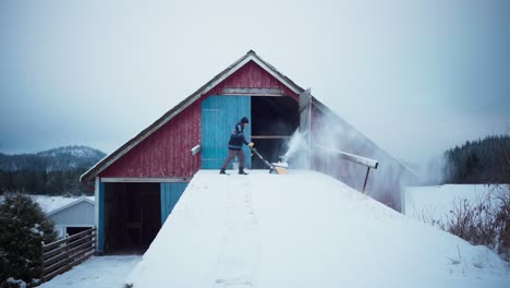 Un-Hombre-Con-Un-Quitanieves-Eléctrico-Quitando-Hielo-Cerca-De-Una-Casa-De-Granero-De-Madera