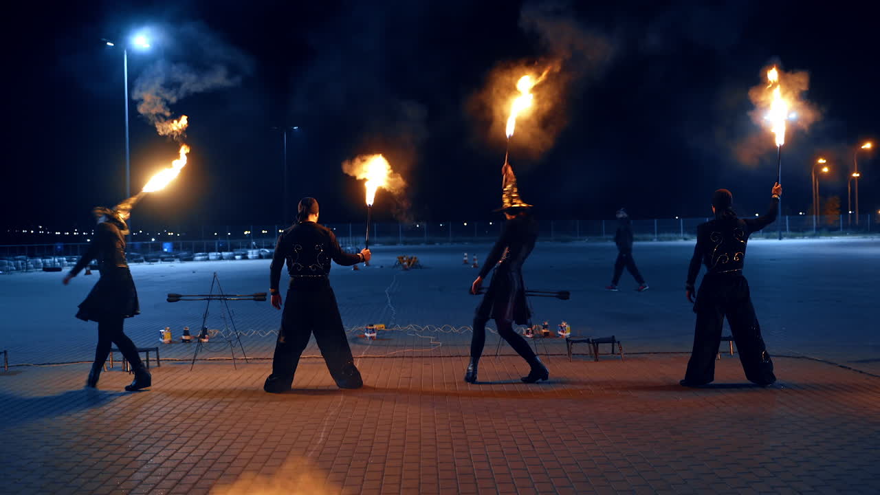 Two men and two women are dancing with burning torches. Group of artists perform fire show outdoors.