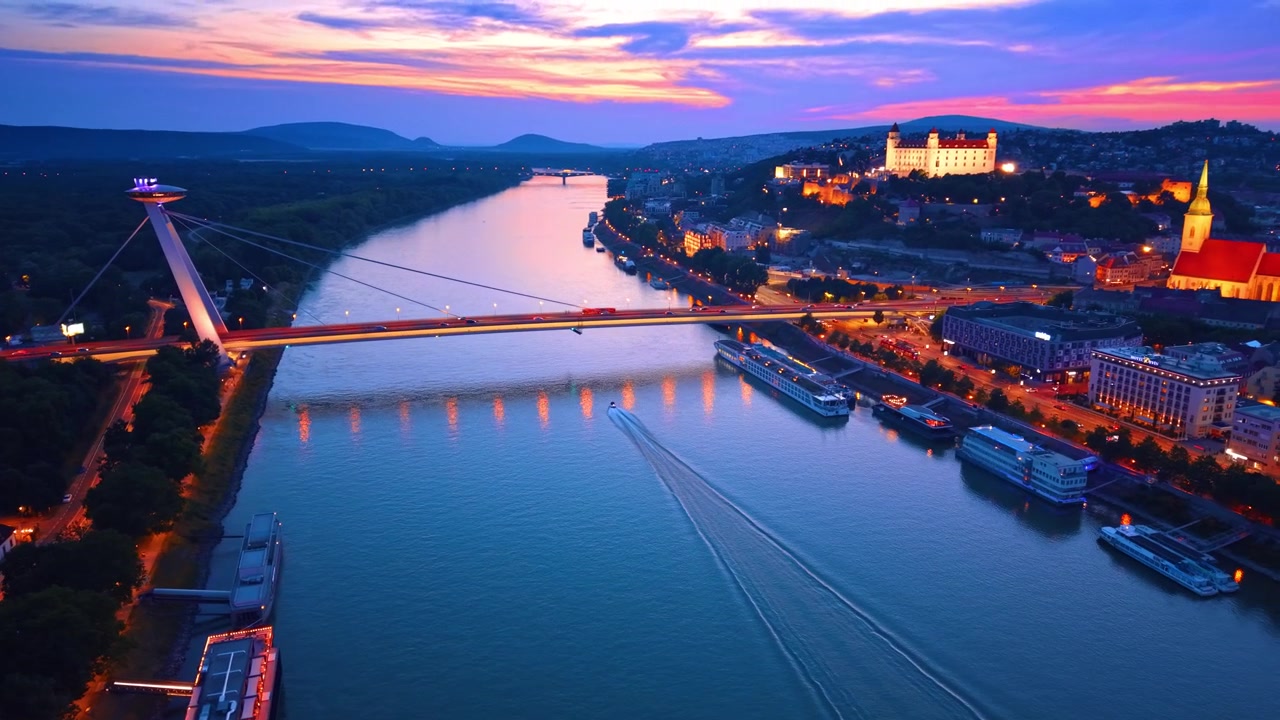 Natligt luftfoto af det oplyste Bratislava Slot og kabelbro. Natligt luftfoto af oplyst slot, skråstagsbro over floden, byens lys og fortøjede skibe i Bratislava.
