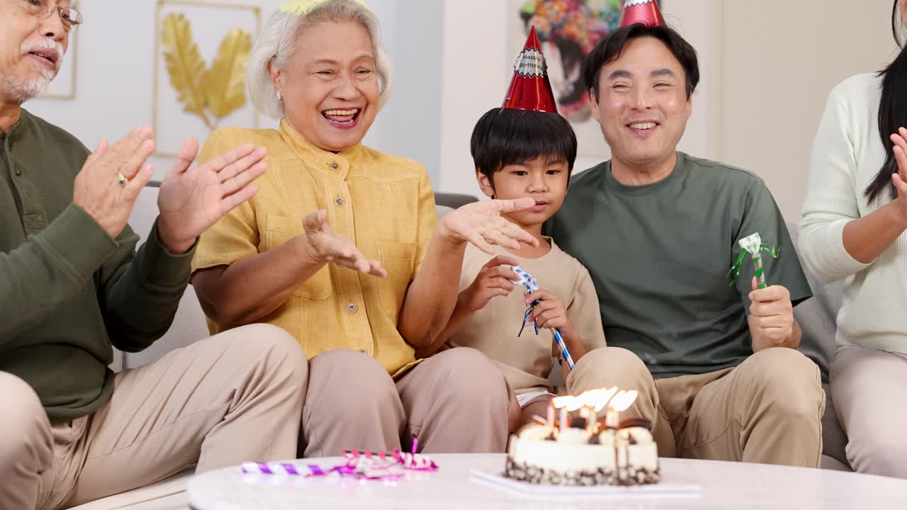 Family gathered around a birthday cake, celebrating with laughter and party hats in a warmly lit room