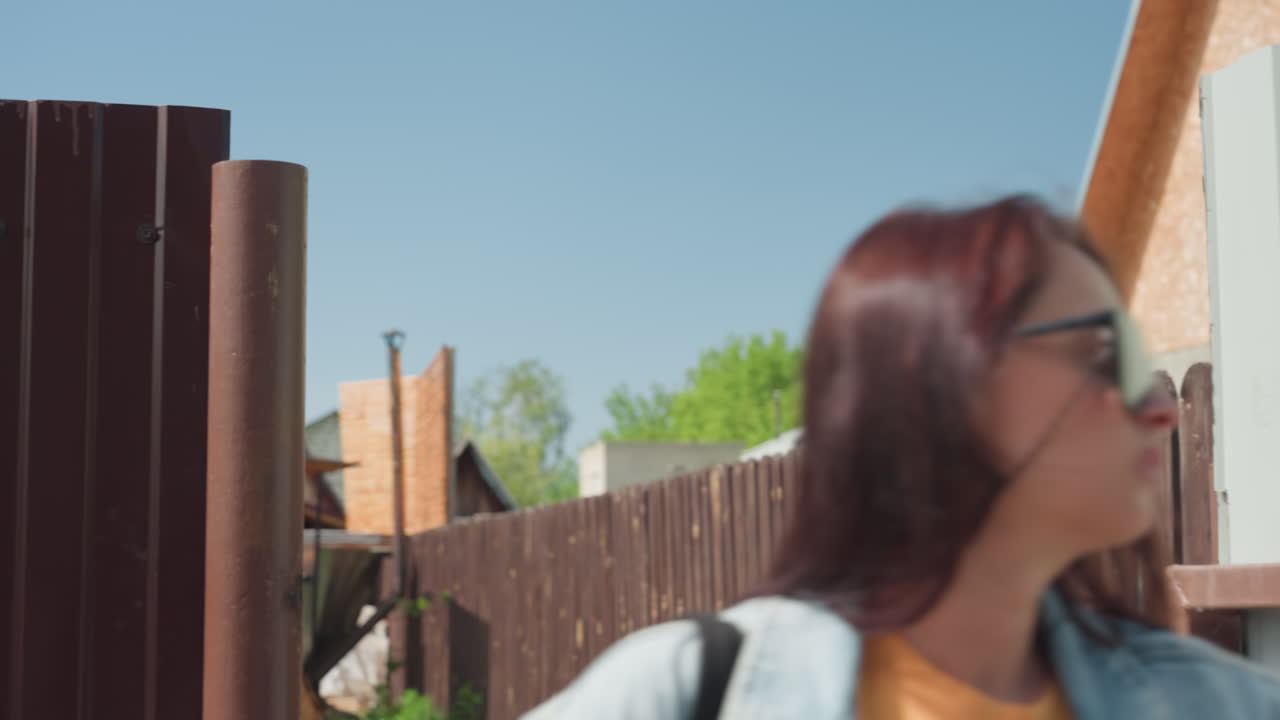 Young girls walk past brown wooden door on sunny day as last person closes door behind her, pauses for a deep breath, and continues walking with thoughtful expression in residential area