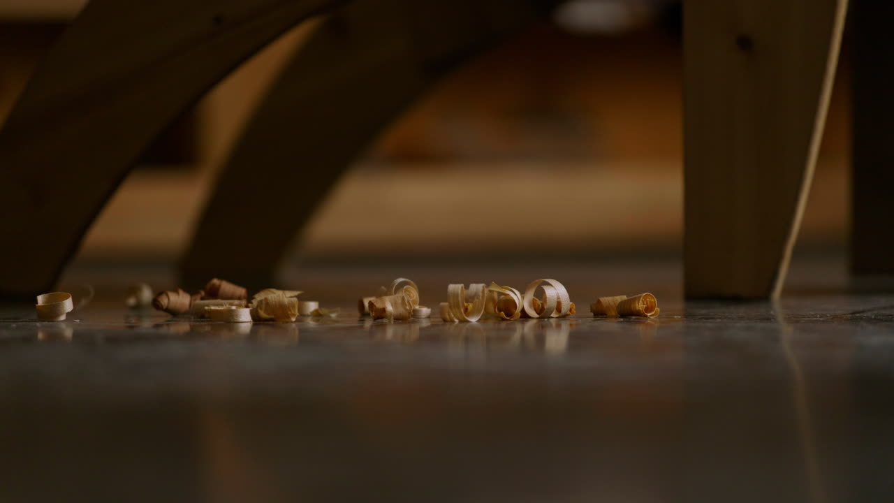 Small curls of wood shavings lie scattered on a clean workshop floor, illuminated by warm afternoon sunlight filtering through nearby windows