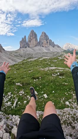 man claps and spreads hands in awe as he swings legs from cliff ledge, tre cime
