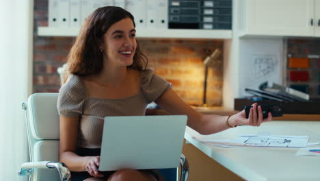 Joven-Empresaria-Sonriente-Trabajando-En-Una-Computadora-Portátil-En-El-Escritorio-De-La-Oficina-Hablando-Por-Teléfono-Móvil