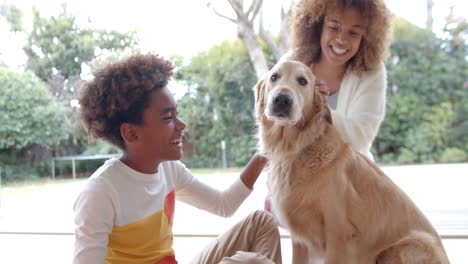 happy african american mother and son sitting on floor, petting dog, slow motion