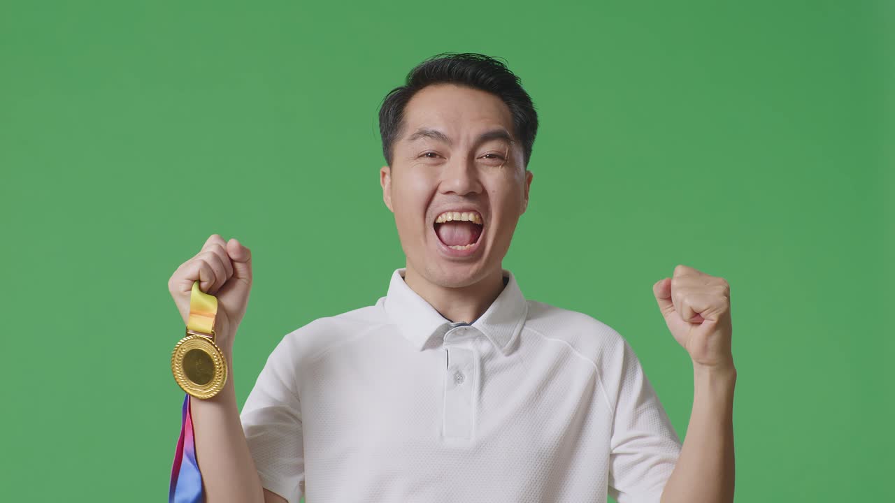 금메달을 바라보는 아시아 남자의 클로즈업, 그 다음에는 울부는 골, 스튜디오의 녹색 스크린 배경에서 첫 번째 우승자로 우승을 축하합니다.
