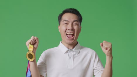 close up of asian man looking at a gold medal then screaming goal celebrating winning as the first winner on green screen background in the studio