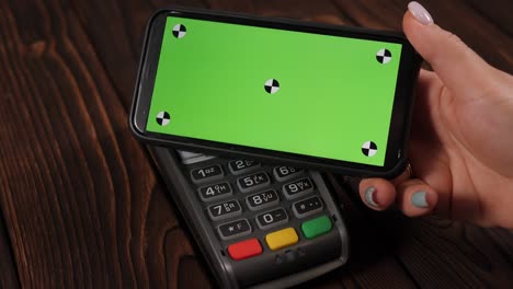 close-up of a woman paying for a purchase using a phone with a green screen. nfc