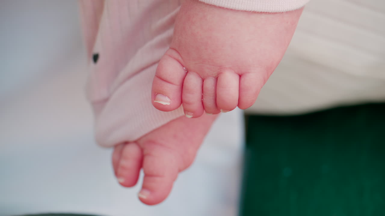 Close up shot of a baby's feet resting on a bench, wearing soft pink clothes with small heart patterns
