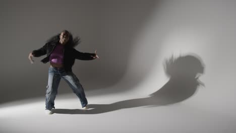 retrato de estudio de larga duración de una mujer joven bailando proyectando sombras con iluminación baja contra un fondo gris 1