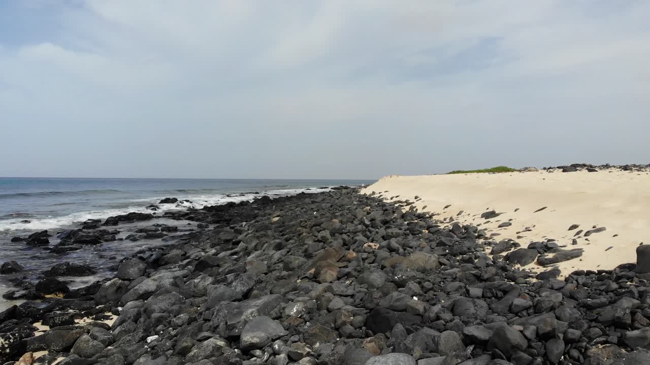 케이프 베르데의 모래 해변 옆에 방파제를 만드는 어두운 바위 위로 공중 저공 비행