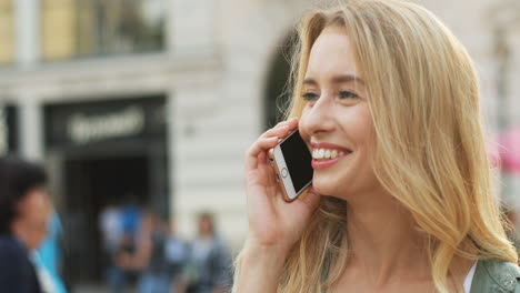 close-up view of caucasian blonde woman talking on the smartphone and laughing in the street