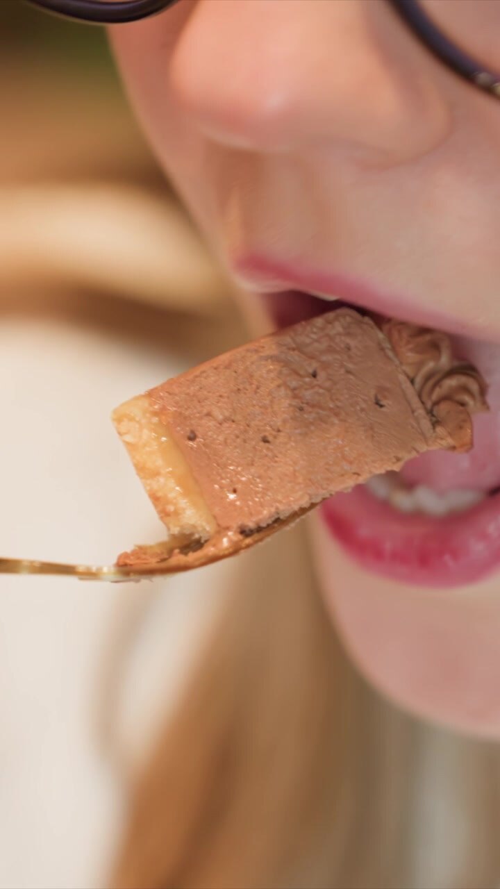 Close up shots show pieces of chocolate cake on fork. woman with pink lipstick and glasses brings food to her mouth taking small bites dessert eating closeup