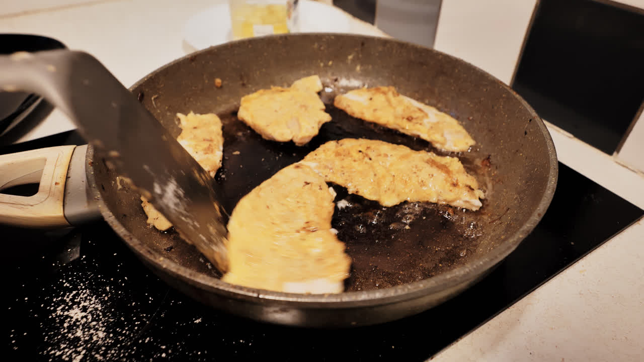 Real-life home cooking moment with chicken fillets frying on cluttered stovetop