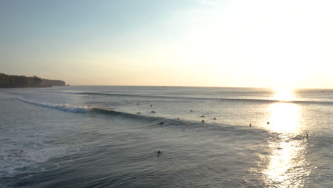 drone flyover surfers in middle of ocean sitting on surfboard watching beautiful sunset in bali indonesia