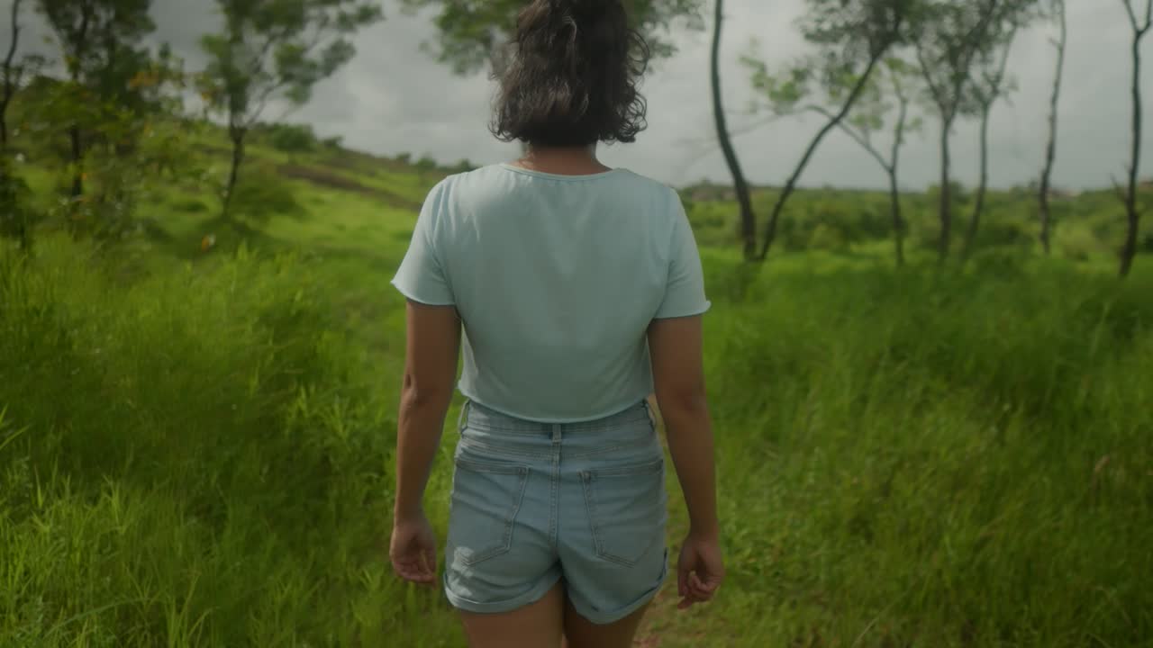 Sow-motion, an unrecognizable young Indian teenage girl gracefullywalks through a lush forest with diverse, vibrant vegetation