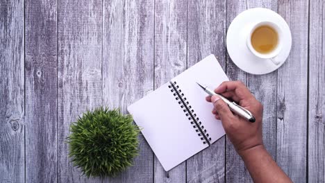 persona escribiendo en un cuaderno con té en una mesa de madera