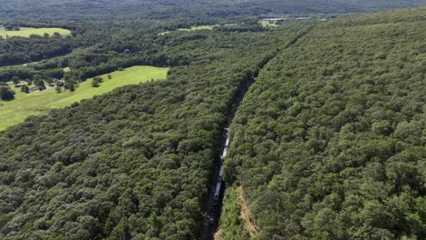 An-aerial-view-of-a-silver-commuter-train-in-the-mountains-of-Cornwall,-NY-on-a-sunny-day