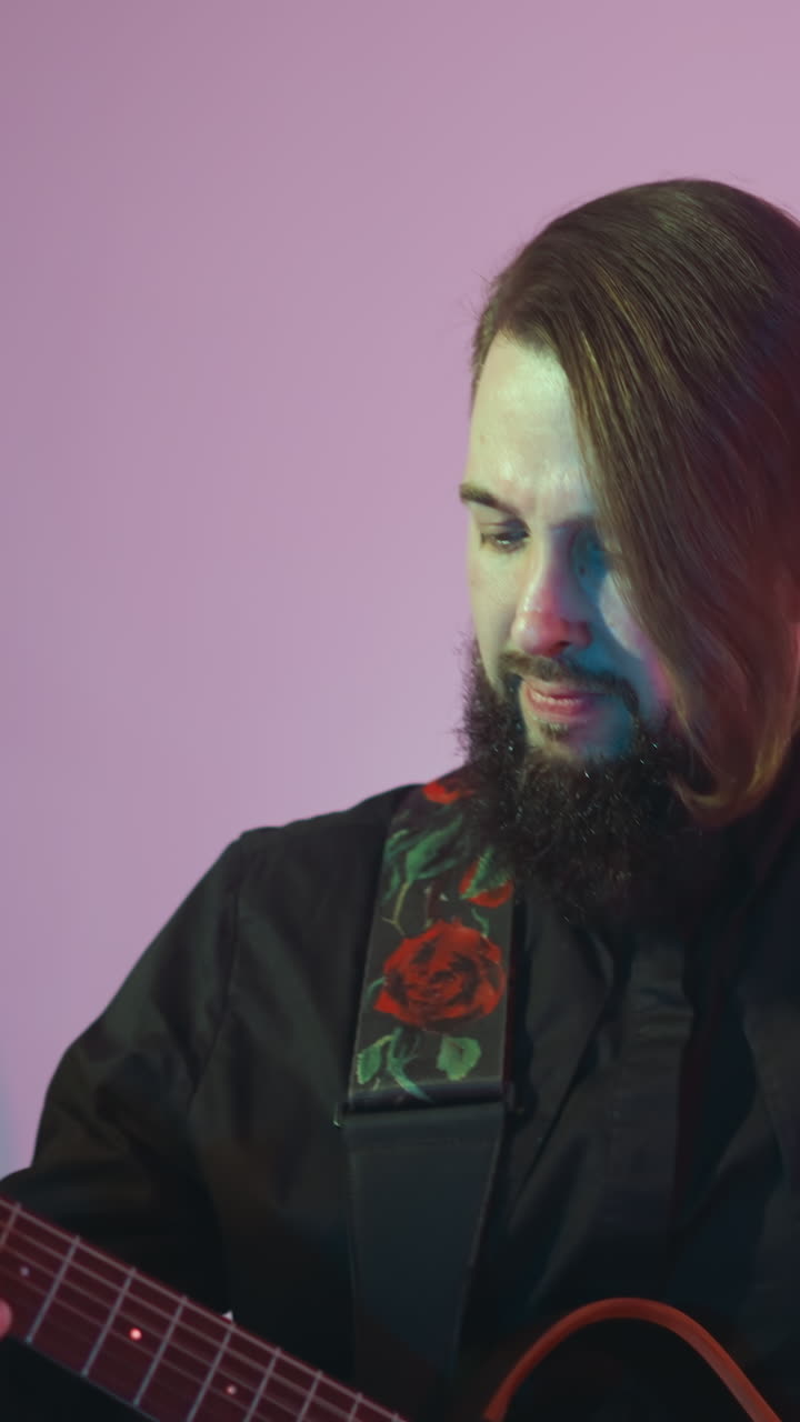 guitarrista barbudo en una camisa negra tocando apasionadamente una guitarra roja, moviendo sutilmente su cabeza contra un fondo blanco con un suave gradiente de luz rosa y azul