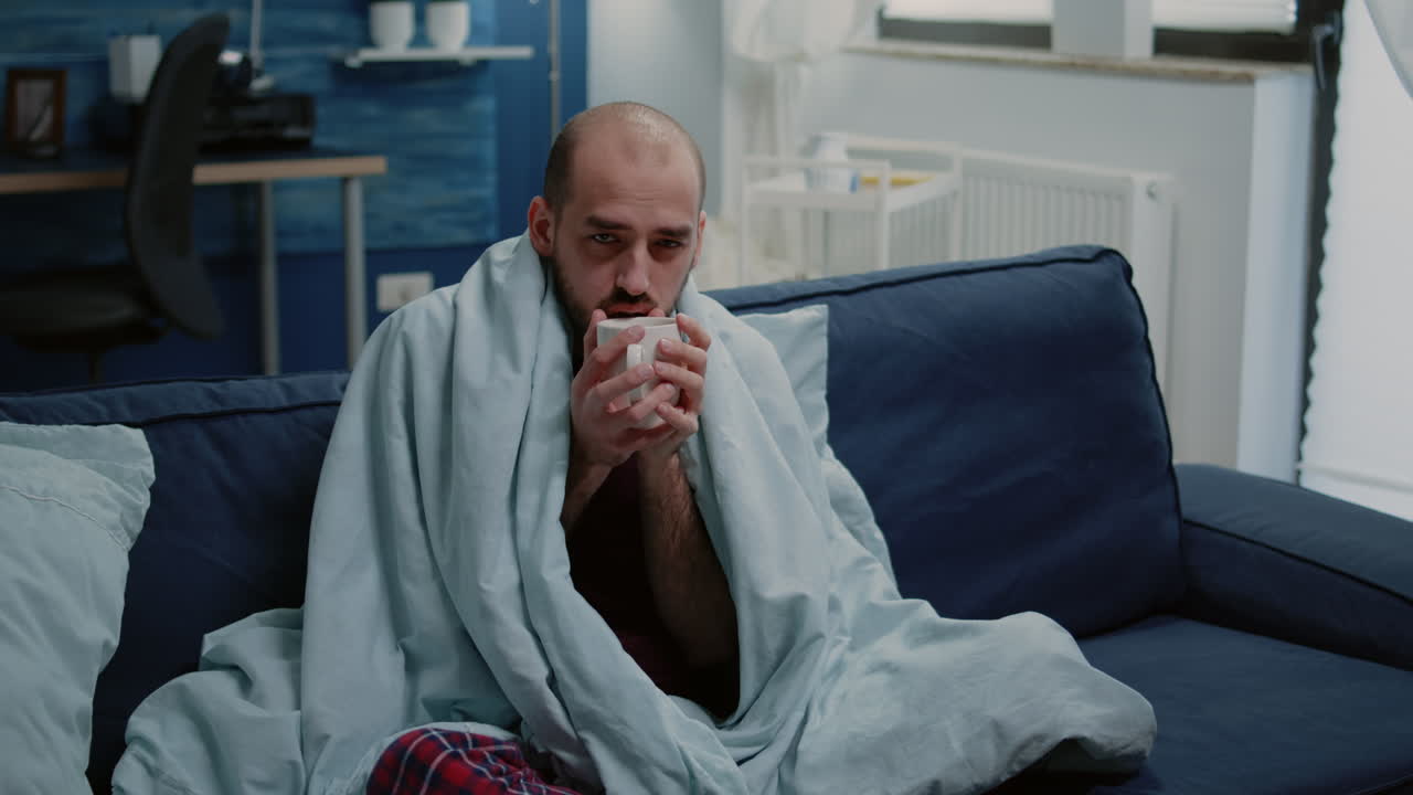 Sick man holding cup of tea and looking at camera