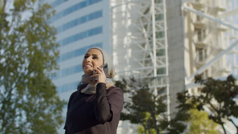 beautiful arab woman in hijab talking on phone outside the building