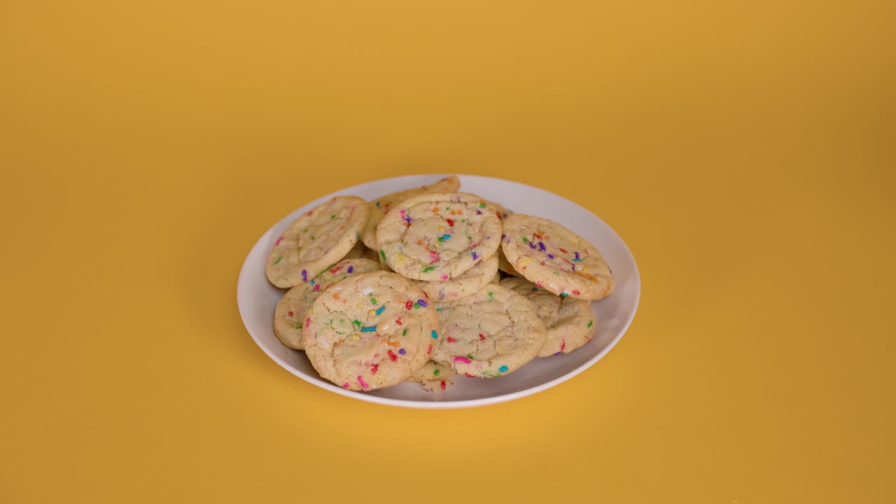 Freshly baked sugar cookies with sprinkles arranged on a bright yellow backdrop
