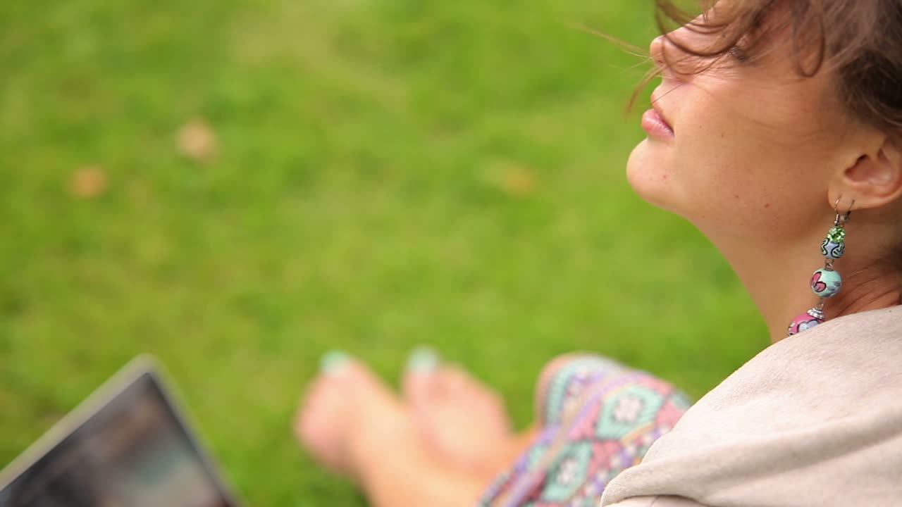 노트북을 사용하여 잔디에 앉아있는 예쁜 젊은 학생