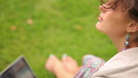 Pretty-young-student-sitting-on-grass-using-laptop