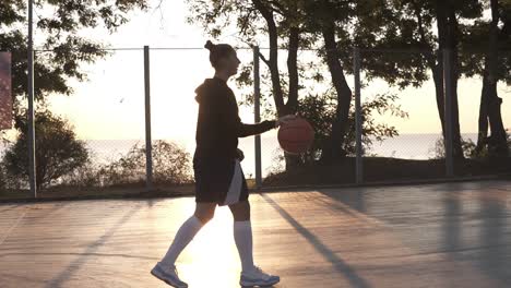 Junge-Basketballspielerin,-Die-Morgens-Am-Basketballplatz-Im-Freien-Vorbeigeht,-Während-Sie-Den-Ball-Hüpft